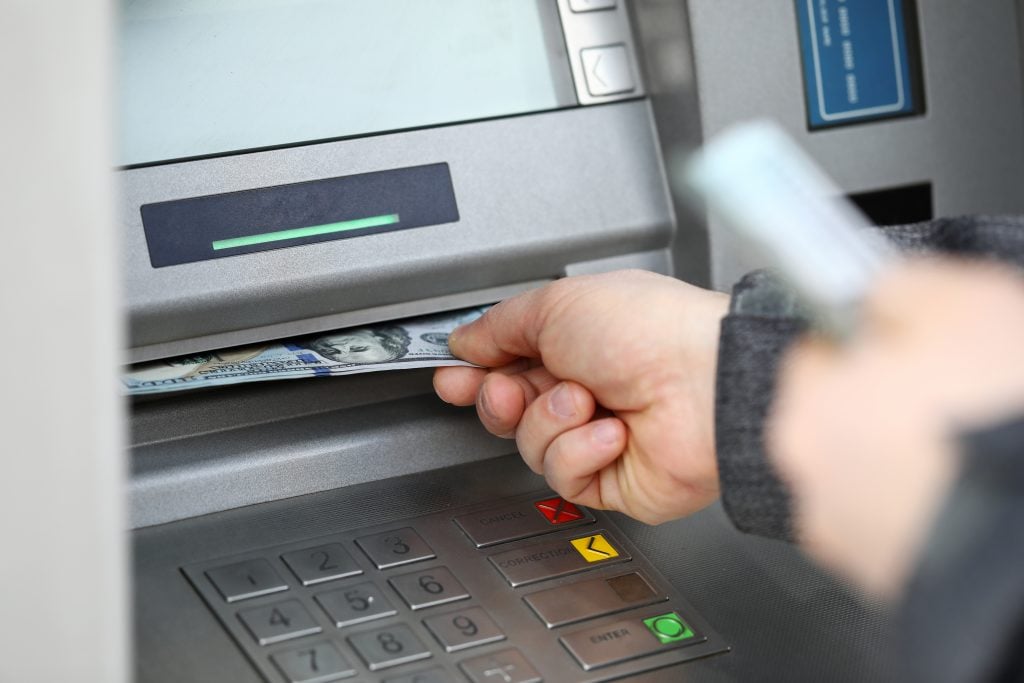 A person is withdrawing USD from an ATM Machine